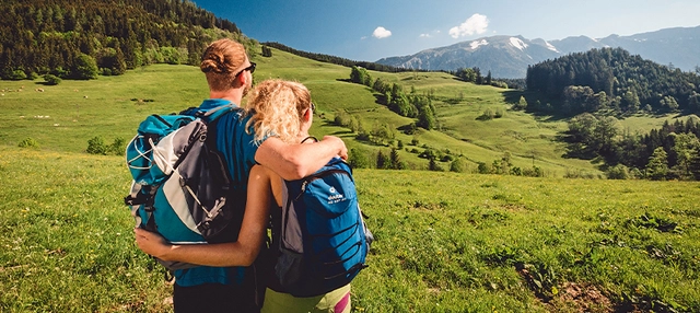 Pärchen Arm in Arm im Grünen vor einer Bergkulisse.