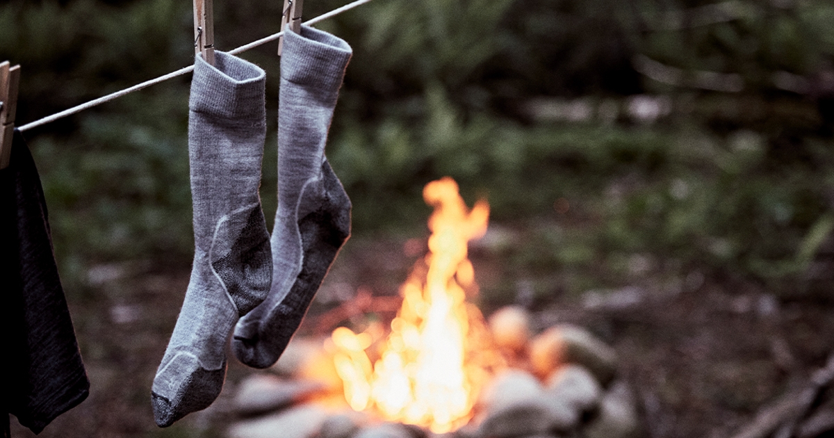 Wandersocken, die an einer Wäscheleine aufgehängt sind, mit Lagerfeuer im Hintergrund.