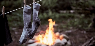 Wandersocken, die an einer Wäscheleine aufgehängt sind, mit Lagerfeuer im Hintergrund.