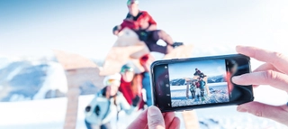 Nahaufnahme eines Handys, das ein Foto von vier Personen in Ski amadé macht.