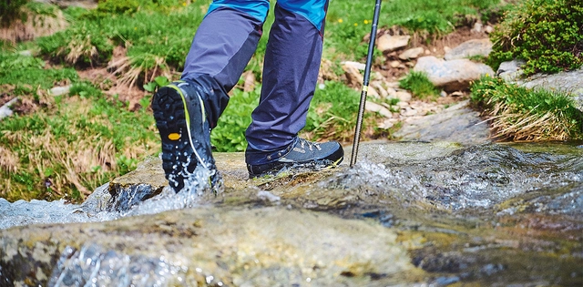 Wanderer mit blauen Wanderschuhen auf tritt auf einen Stein. Wasser spritz auf.