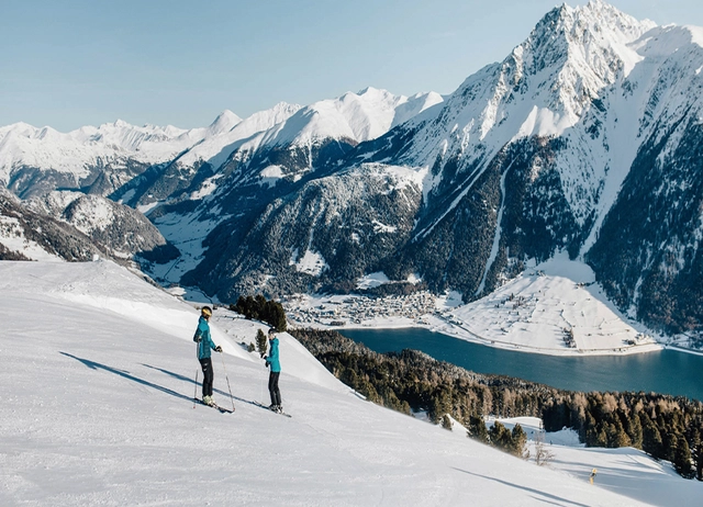 Zwei Skifahrer auf der Piste vor verschneiten Bergen in der Zwei Länder Skiarena.