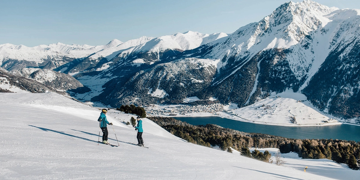 Zwei Skifahrer auf der Piste vor verschneiten Bergen in der Zwei Länder Skiarena.