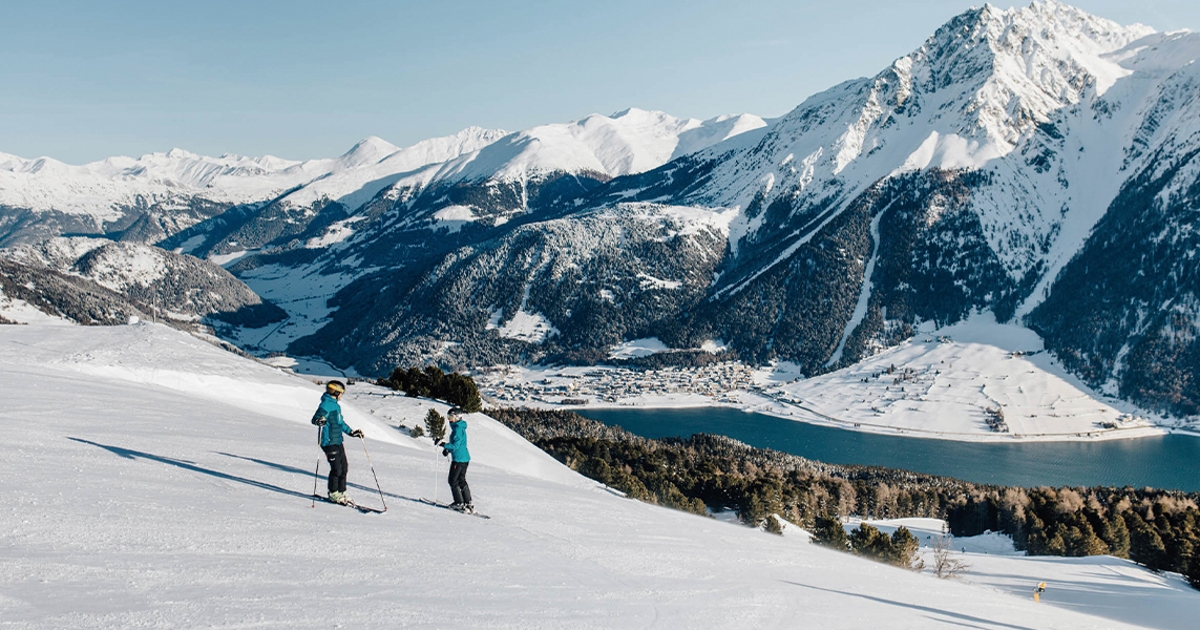 Zwei Skifahrer auf der Piste vor verschneiten Bergen in der Zwei Länder Skiarena.