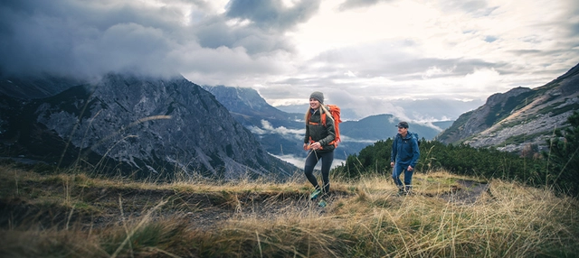 Zwei Wandernde vor Bergpanorama.