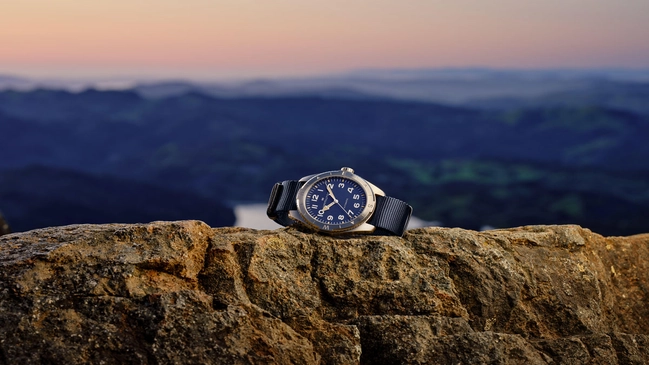 Hamilton Khaki Field Expedition 41 mm mit blauem Zifferblatt und blauem NATO-Band liegend vor Landschaft