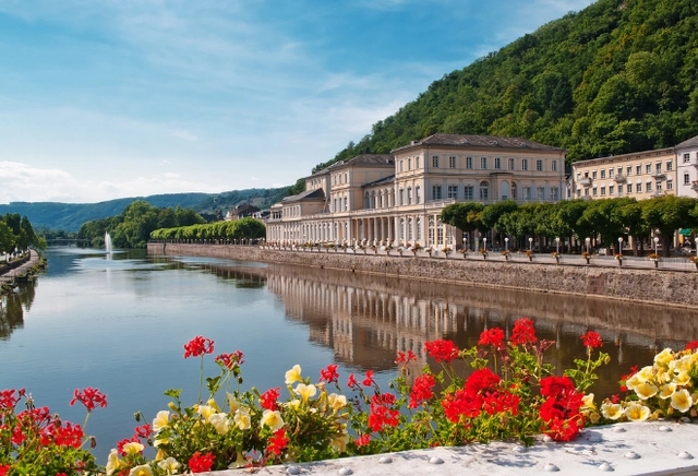 Ein großes Gebäude direkt am Fluss mit blühenden Blumen direkt davor