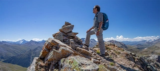 Wanderer stehend auf Felsvorsprung mit Blick auf Bergpanorama.