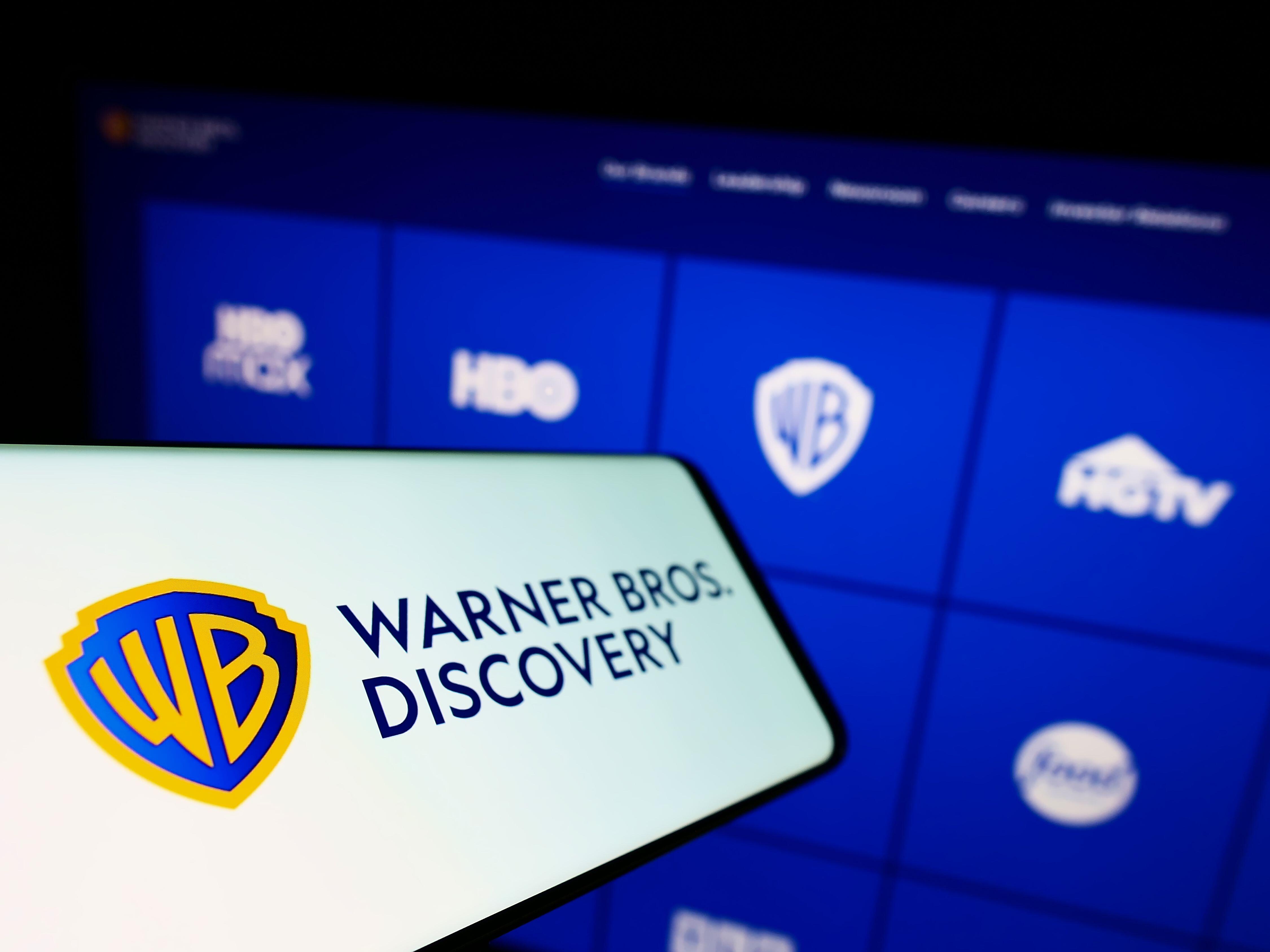 Mobile phone with Warner Bros. Discovery logo on screen in front of business website