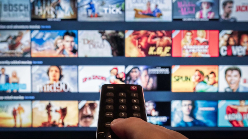 TV television displaying streaming content with hand holding a remote in the foreground