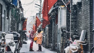 Two people using a phone on a snowy street lined with Chinese flags