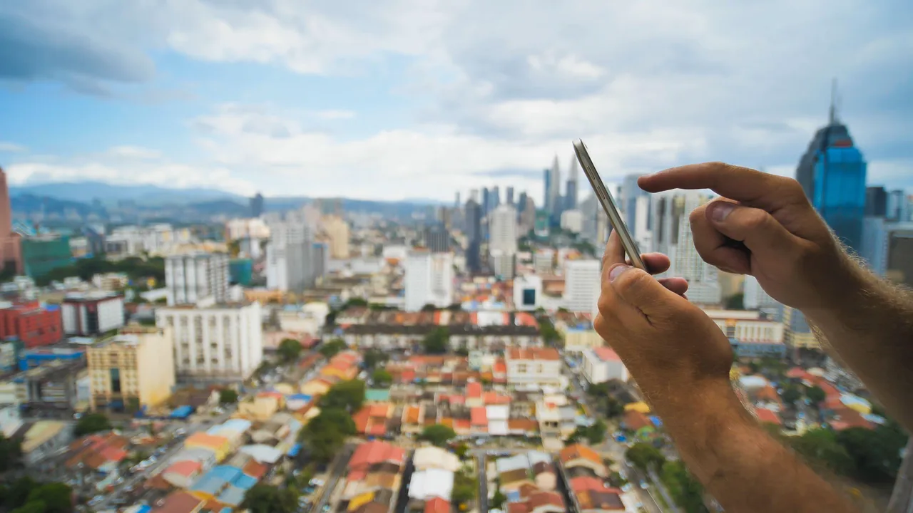 Hands holding a phone with Kuala Lumpur, Malaysia in the background Hands holding a phone with Kuala Lumpur, Malaysia in the background