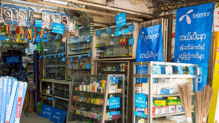 Hardware store with signs and banners for the Norwegian telecom group Telenor at Bagaya Street in Yangon, Myanmar. (Source: Jorgen Udvang / Alamy Stock Photo)
