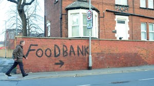 Man walking pastd a foodbank sign on a wall