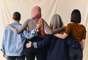 Rear view of four women with arms around each other in support of International Women's Day.