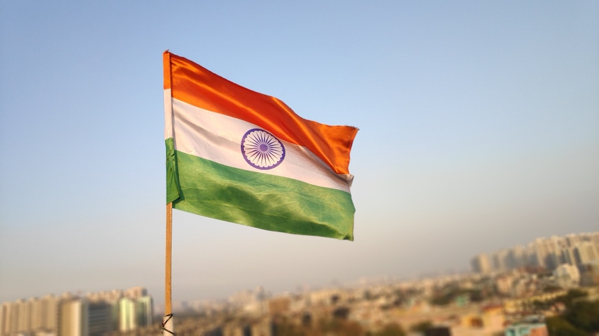 Indian flag with blue sky and buildings in background.