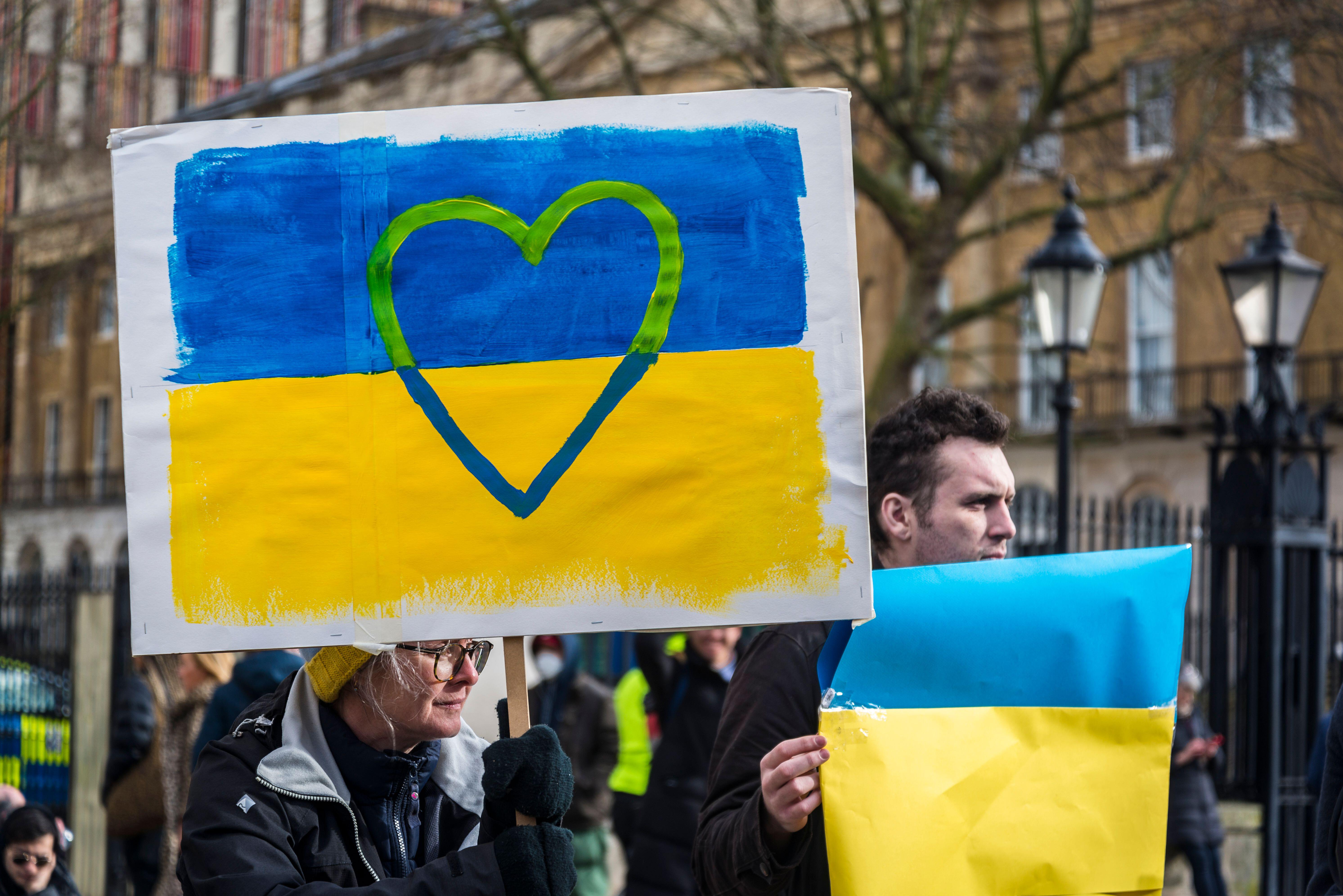A person holding a sign painted like the Ukraine flag with a heart over it