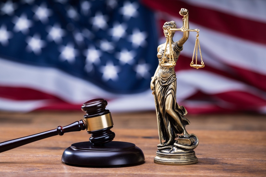 Gavel with golden scales on table in front of a US flag 