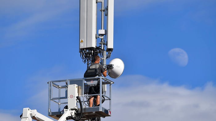 Cell tower on a house roof in Germany. Worker stands on a lifting platform and works on an antenna mast. (Source: pa picture alliance / Alamy Stock Photo)