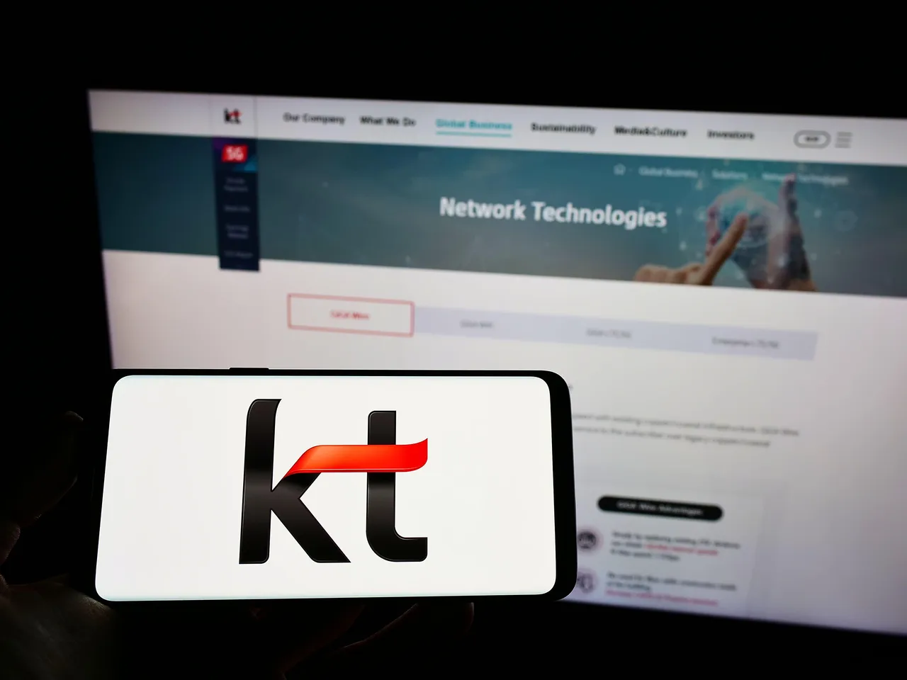 KT Corp logo on a smartphone, with the website on a screen in the background KT Corp logo on a smartphone, with the website on a screen in the background