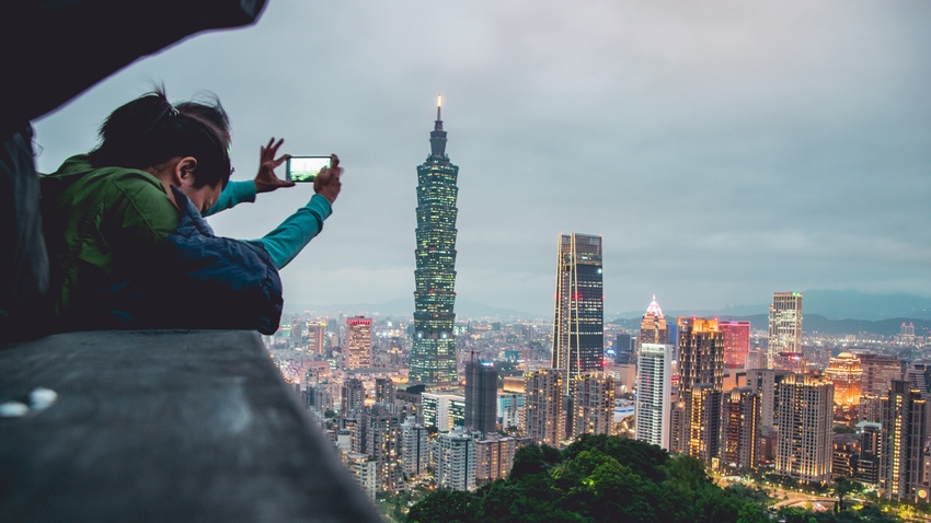 A person using a phone to take a picture of the Taipei skyline.