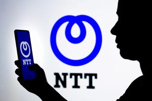 Person holding a smartphone with NTT logo, another NTT logo in background