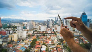 A man's hand holding a smartphone in Kuala Lumpur, Malaysia, with a view of the city in the background.