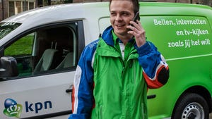 A KPN worker talking on the phone and standing in front of a KPN branded car