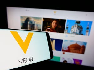 VEON logo on a smartphone, in front of a laptop showing its website.