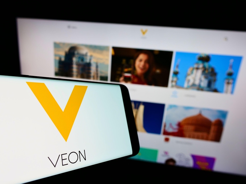 VEON logo on a smartphone, in front of a laptop