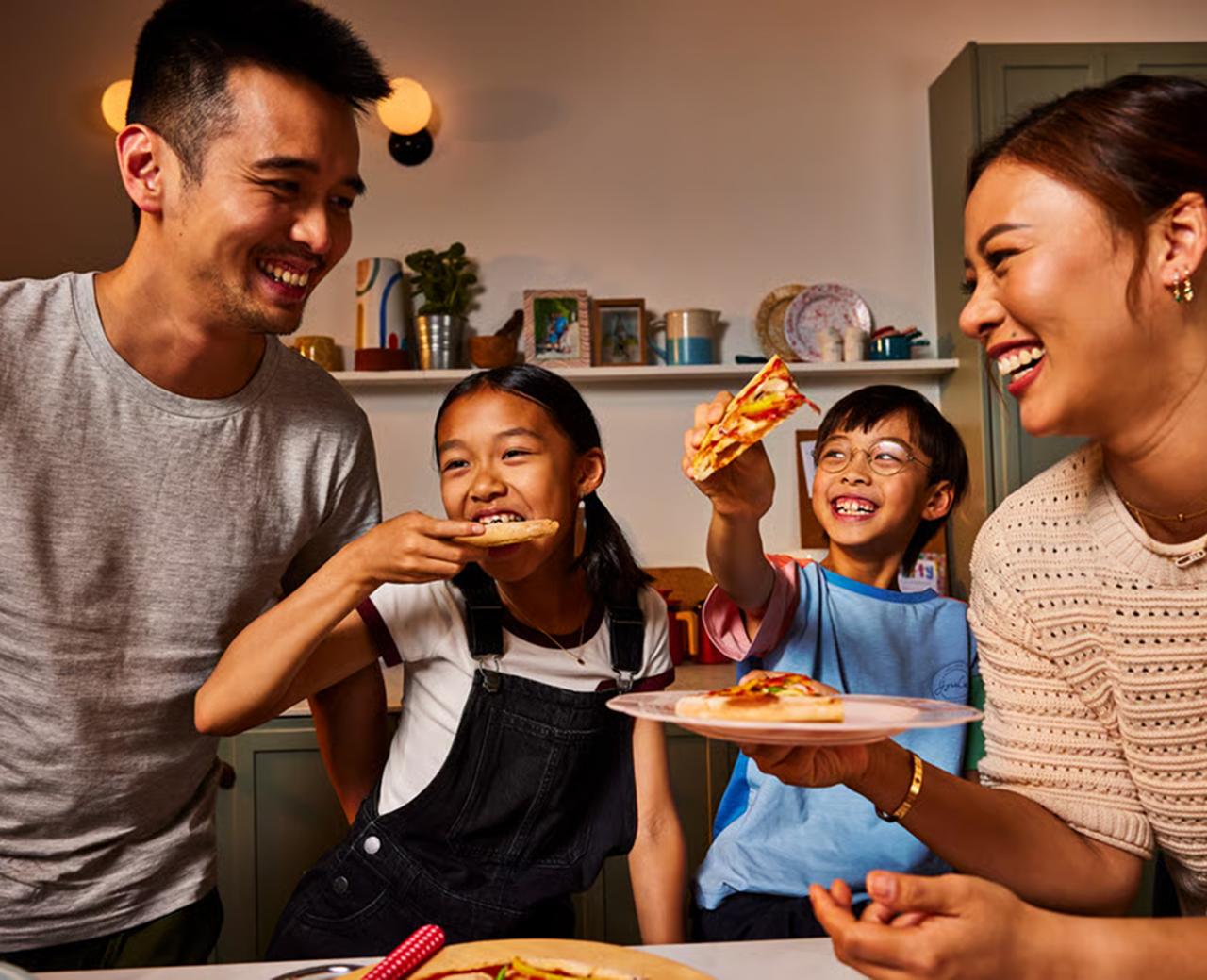 A family of two parents and two young children eating together in the kitchen.