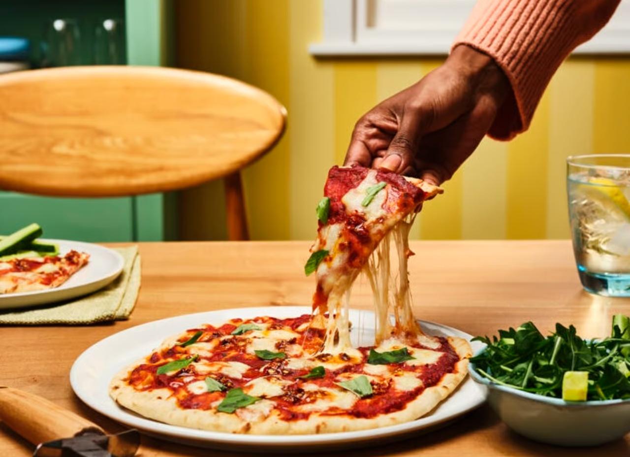 A freshly baked, homemade pizza on the dining table with a slice being pulled, showing the cheesy topping.