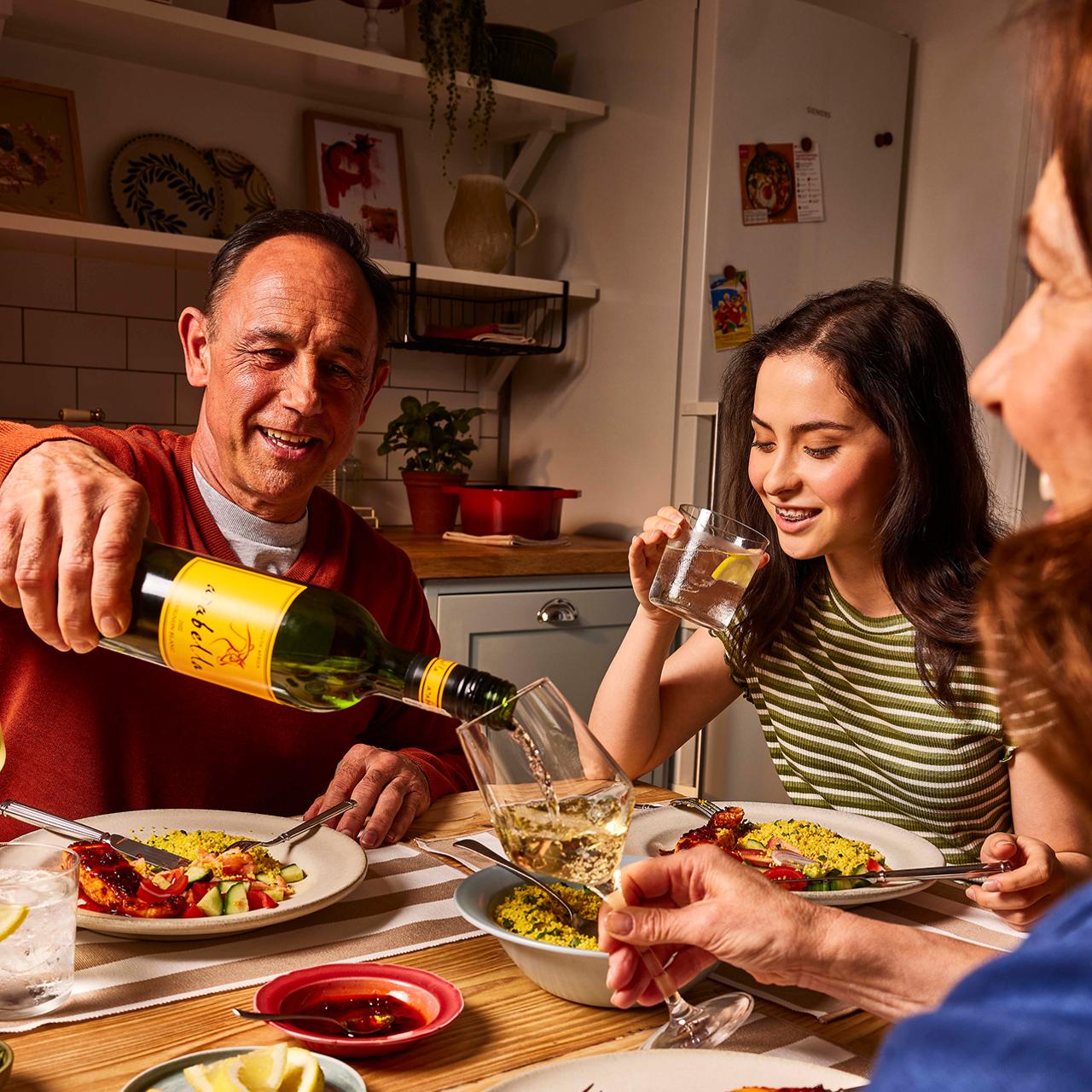 A family of three sitting round the dinner table eating their freshly cooked Gousto meal together.