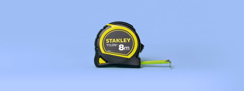 Een zwart-gele rolmaat staat uitgetrokken tegen een lichtblauwe achtergrond, wat precisie en meten suggereert.