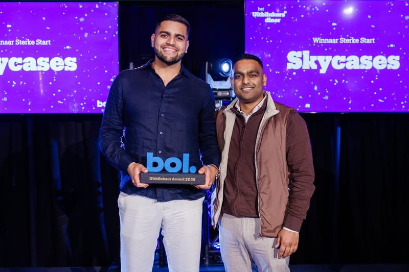 Two men smile and pose with a trophy at an awards ceremony. On purple screens in the background, ‘Skycases’ and festive texts are displayed.