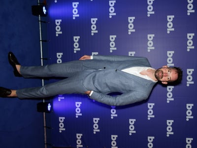 Man in a blue suit and glasses stands on a blue carpet, smiling. The background features a repeated "bol." logo on a matching blue wall.
