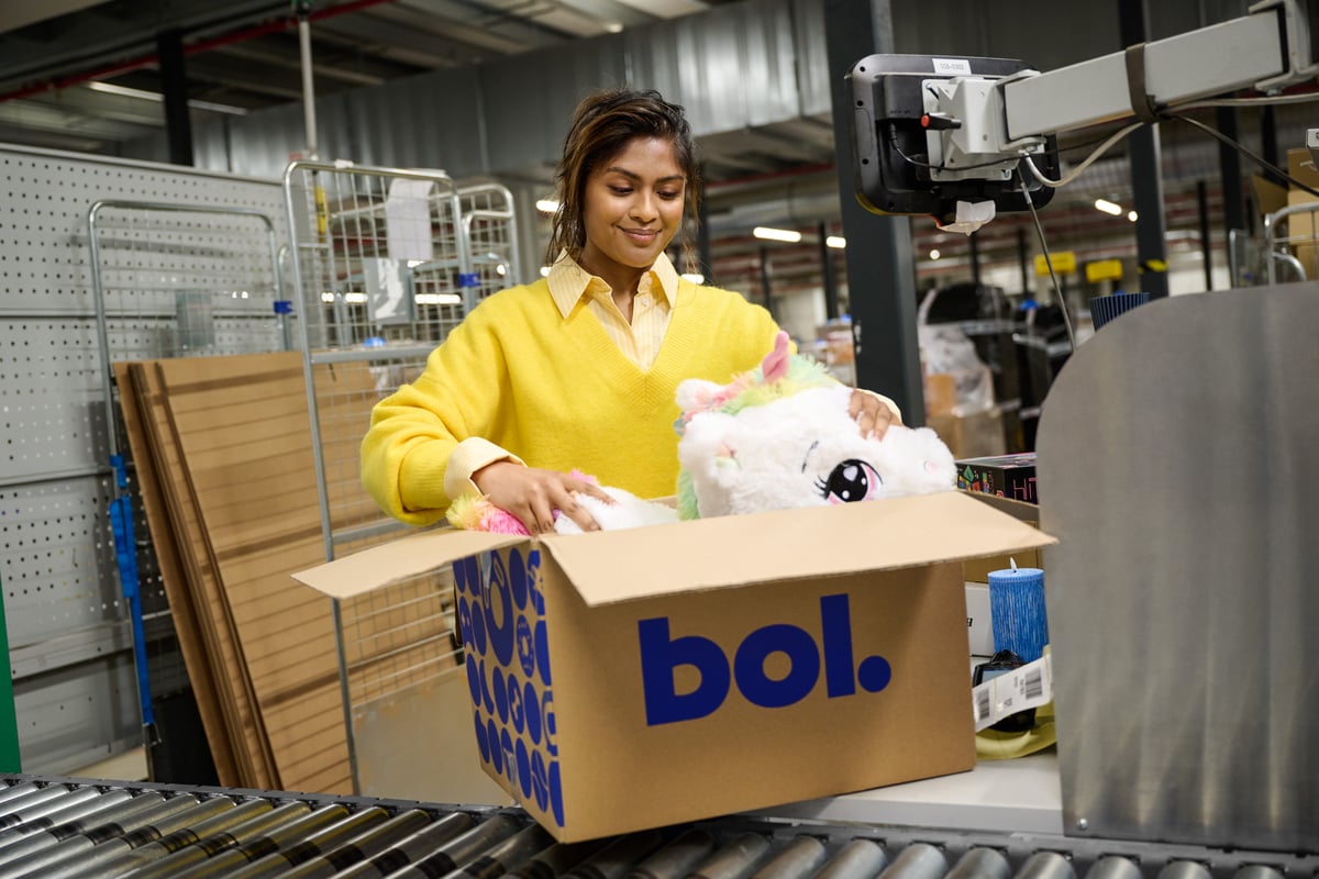 Een glimlachende man en vrouw staan in een magazijn vol dozen en wisselen pakketten uit.