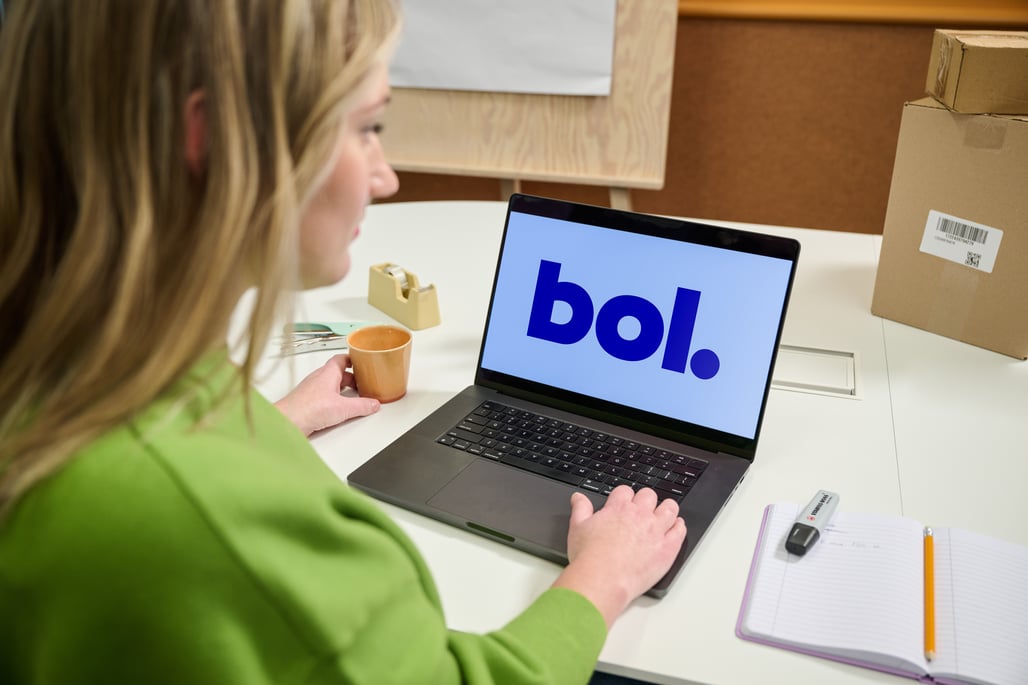 A woman in a green sweater works on a laptop showing 'bol'.