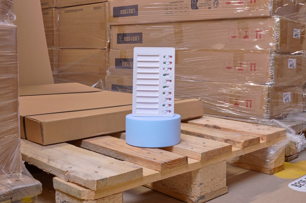 Je ziet een plastic bord met vinkjes als een checklist op een sokkel tussen een stapel pallets en dozen