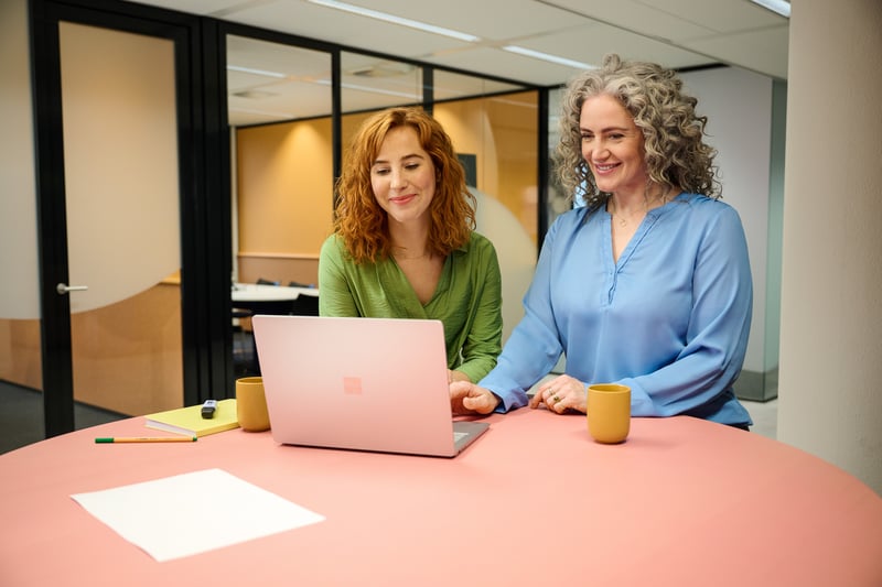 Twee vrouwen staan samen achter een laptop.