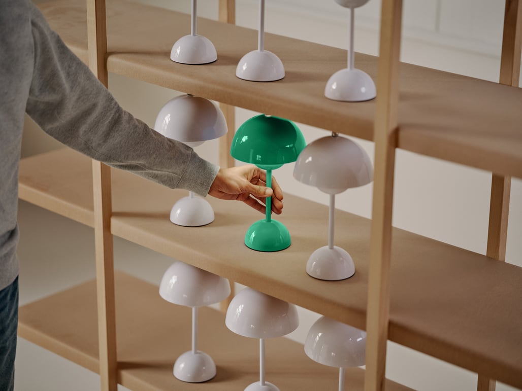 This image shows a set of shelves with white lamps. A hand is reaching for a green lamp.