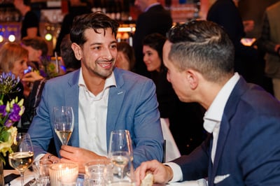 Twee mannen in pakken zijn in gesprek in een restaurant, omringd door gasten.