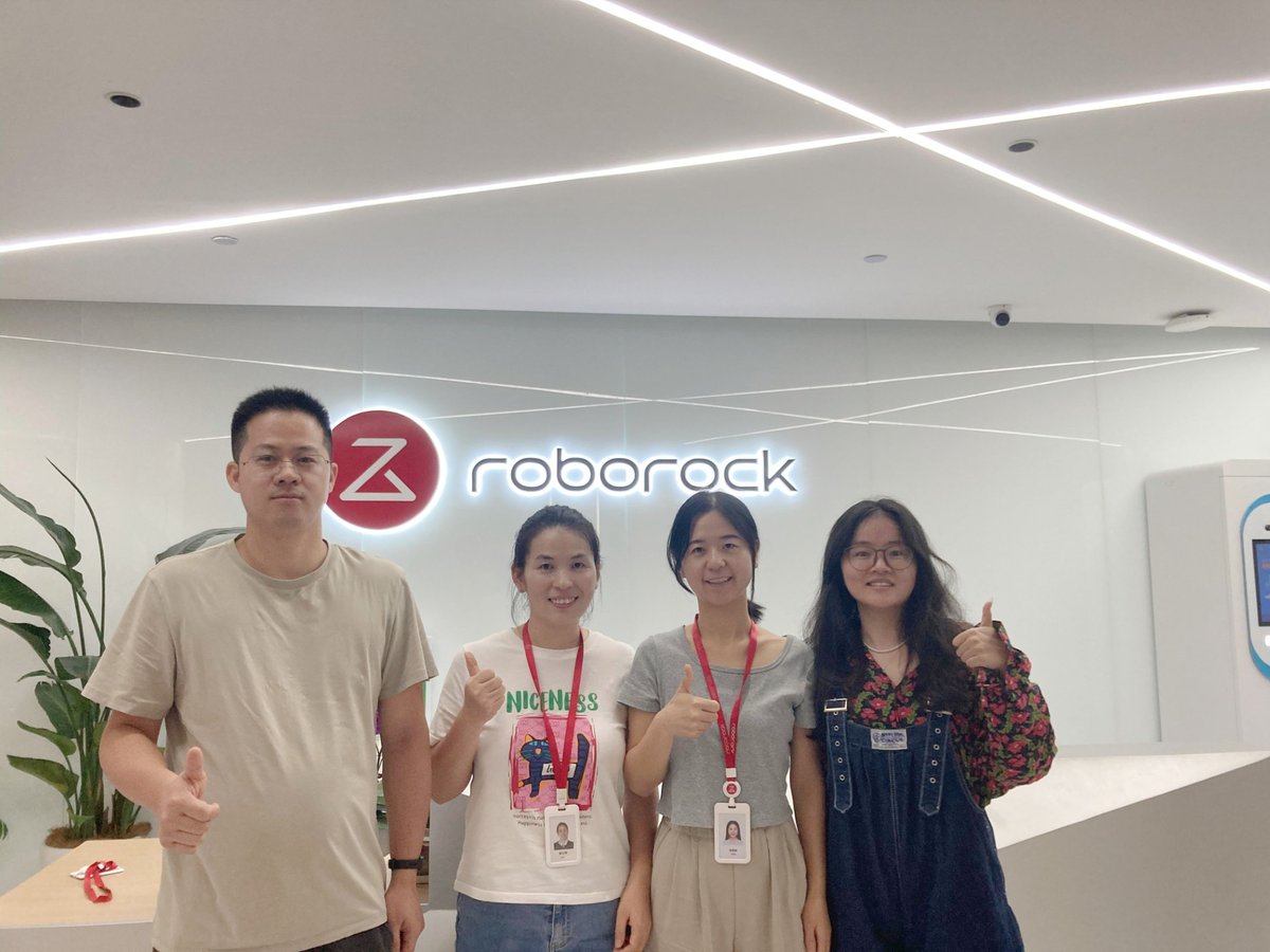 Vier medewerkers van Roborock staan lachend voor het Roborock logo. Ze geven een duim omhoog en stralen een positieve en enthousiaste werksfeer uit.