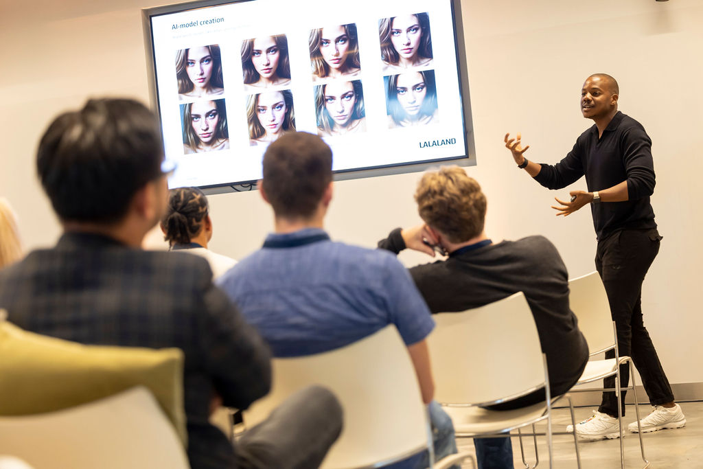 Een presentator spreekt voor een aandachtig publiek en wijst naar een scherm waarop door AI gegenereerde modelafbeeldingen worden getoond. De setting is een moderne vergaderzaal.