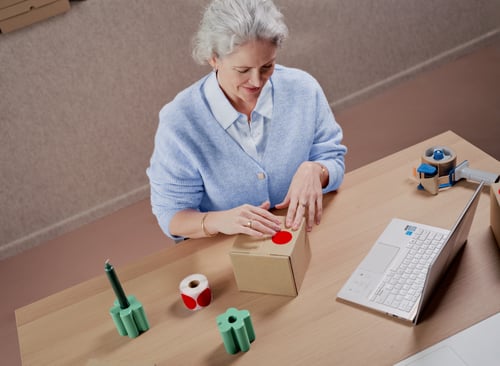 Une femme emballe un colis avec un autocollant rouge sur le dessus.