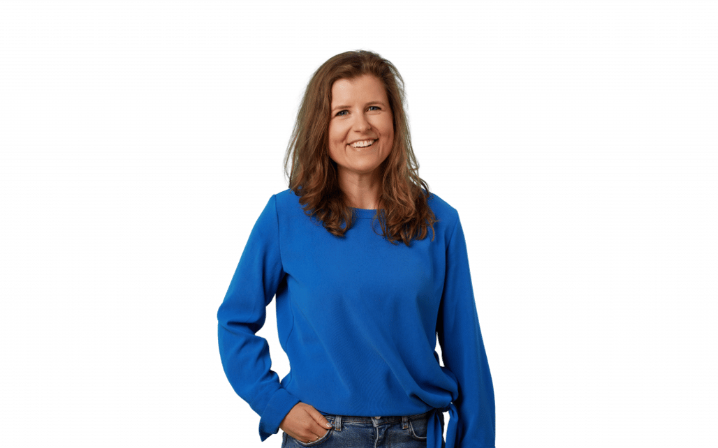 Smiling woman in a blue sweater stands against a black background, hand in pocket.