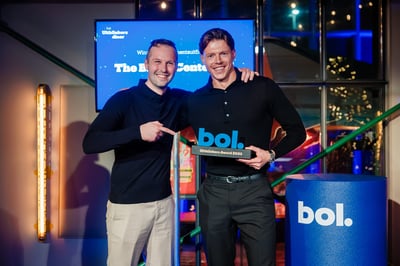 Twee glimlachende mannen staan samen in een feestelijke setting, waarvan één met een trofee met de tekst ‘bol. Uitblinkers Award 2023’ in zijn handen