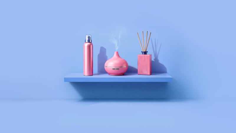 A blue shelf with a pink shower foam bottle, a steaming pink aroma diffuser, and a pink scent diffuser.