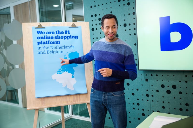 Een man in een blauwe trui wijst naar een poster op een schildersezel, waarop wordt getoond dat bol de nummer 1 marketplace in Nederland en België is.