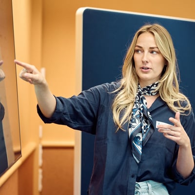 Een vrouw wijst naar een whiteboard.